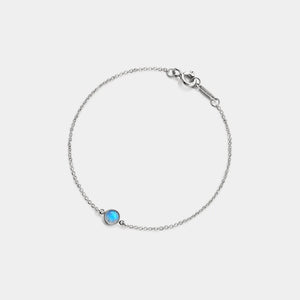 Silver bracelet with a blue gemstone on a light gray background