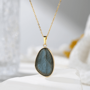 Gold necklace with a teardrop-shaped labradorite pendant on a white surface.