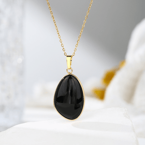 Gold necklace with a black teardrop pendant on a soft white background
