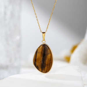 Gold necklace with a tiger's eye pendant on a white surface
