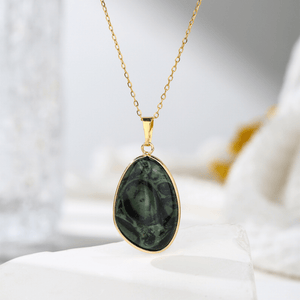 Gold necklace with a green pendant on a white surface
