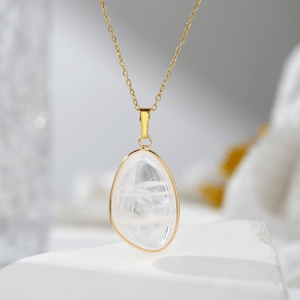 Gold necklace with a clear teardrop pendant on a soft white background