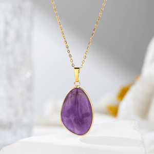 Gold necklace with a purple teardrop pendant on a soft white background