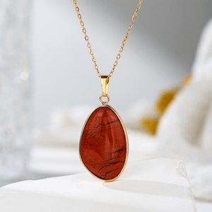 Gold necklace with a red stone pendant on a white surface