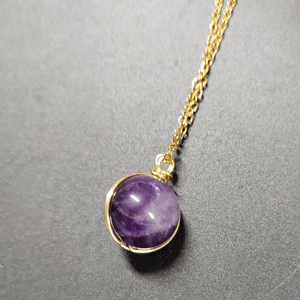 Purple gemstone pendant on a gold chain against a gray background