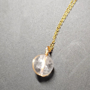 Necklace with a clear crystal pendant on a gold chain against a gray background