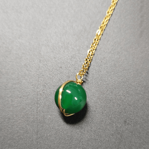 Green jade pendant on a gold chain against a gray background