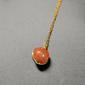 Necklace with a round brown pendant on a gold chain against a gray background