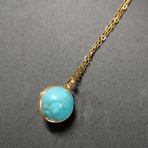 Turquoise pendant necklace on a gold chain against a gray background