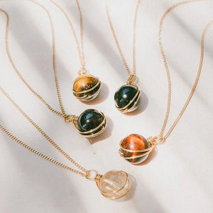 Three gold necklaces with gemstone pendants on a light fabric background