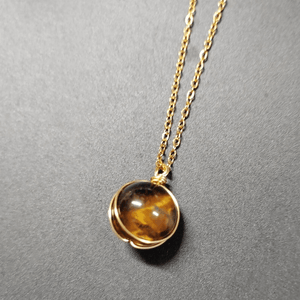 Gold necklace with a round amber pendant on a gray background