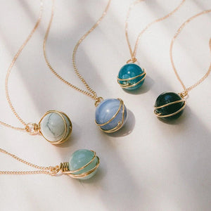 Gold necklaces with various colored stone pendants on a light background