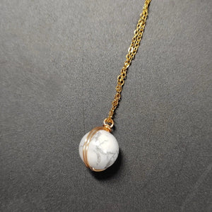 Necklace with a white marbled pendant on a gold chain against a gray background
