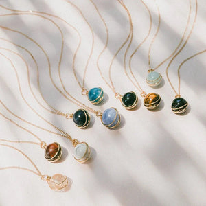 Gold necklaces with various gemstone pendants on a textured white surface