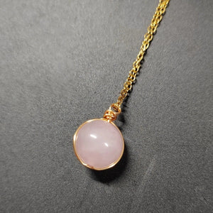 Necklace with a pink pendant and gold chain on a gray background