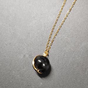 Necklace with a black pendant on a gold chain against a gray background