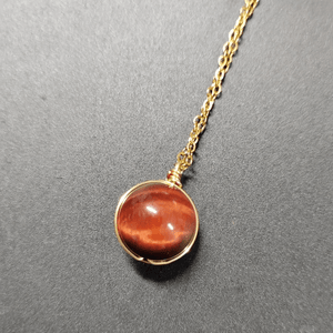 Necklace with a round brown pendant on a gold chain against a gray background