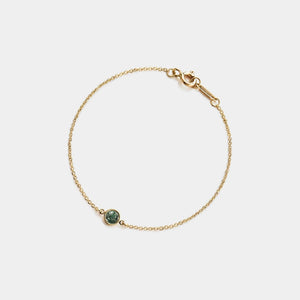 Gold bracelet with a green gemstone on a light gray background