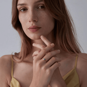 A model wearing a gold bypass ring, featuring a natural opal stone in a thin bypass design.