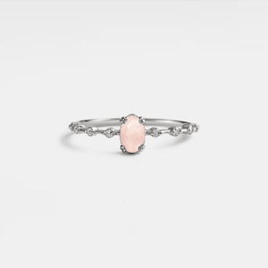 A rose quartz ring with gold plating on a silver band, featuring a single prominent rose quartz oval in the center, flanked by smaller clear stones on either side.