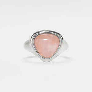 A gold-colored cocktail ring with a rose quartz crystal, set on a plain white background.