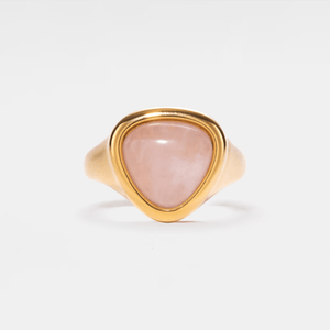 A gold-colored cocktail ring with a rose quartz crystal, set on a plain white background.
