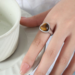 A gold-colored cocktail ring with a raw rose quartz crystal set on a rock, part of a collection.