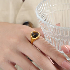 A gold-colored cocktail ring with a raw rose quartz crystal set on a rock, part of a collection.