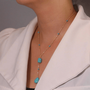 Necklace with turquoise stones worn by a person in a light-colored outfit.