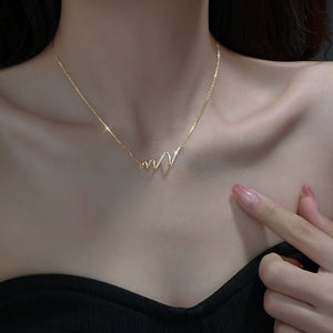Gold necklace with a unique design worn by a person, with a hand pointing to it.