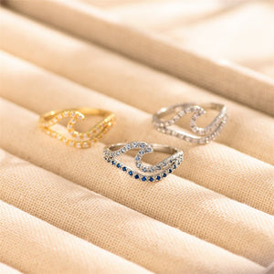 Two rings on a beige fabric surface, one gold and one silver with blue stones.