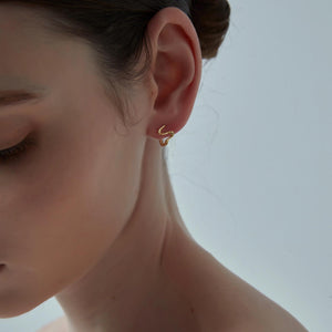 Close-up of a person wearing a gold earring against a neutral background