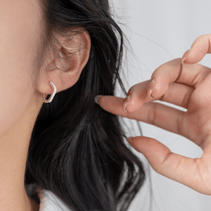 Close-up of a person wearing a silver hoop earring with a neutral background