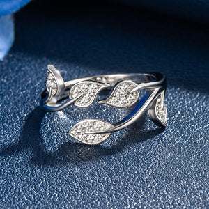 Silver leaf-shaped ring with gemstones on a blue textured background