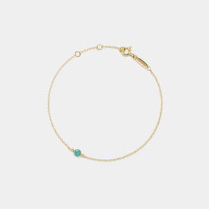 Gold bracelet with a small green gemstone on a light gray background