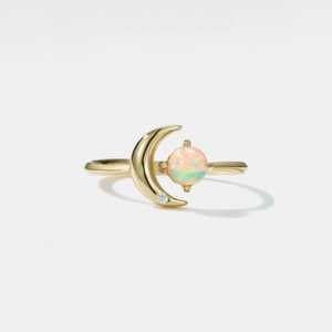 Gold ring with a crescent moon design and opal stone on a light gray background