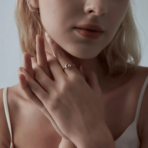 Model wearing a gold ring with a crescent moon design and opal stone on a light gray background