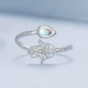 Silver ring with a teardrop-shaped gemstone and hamsa hand design on a light blue background
