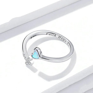 Silver ring with heart-shaped blue gemstone and 'Faith Hope Love' engraving on a white background