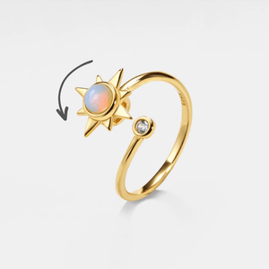 A gold-colored spinner ring featuring a central opal stone with a star design, accompanied by a small cubic zirconia.