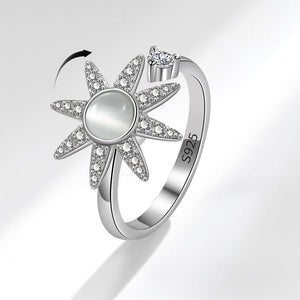 Silver sun-shaped spinner ring with gemstones on a light gray background