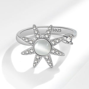 Silver sun-shaped spinner ring with gemstones on a light gray background