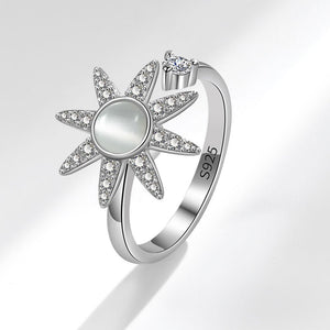 Silver sun-shaped spinner ring with gemstones on a light gray background