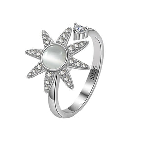 Silver sun-shaped spinner ring with gemstones on a light gray background