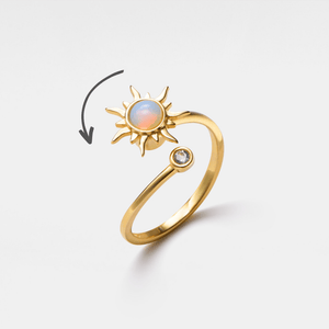 Gold spinner ring with sun design and small gemstone on a light beige background