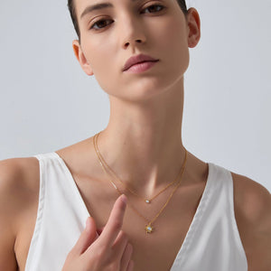 Woman wearing a gold necklace with a small pendant on a plain background