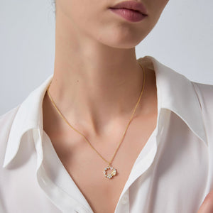 Gold necklace with a pendant worn by a person in a white shirt against a neutral background