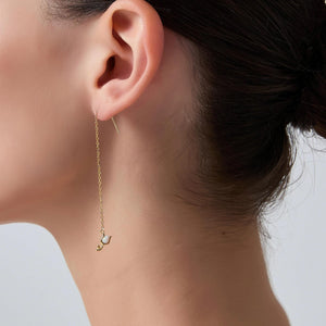 Close-up of a gold earring with a small pendant worn by a person.
