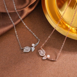 Two necklaces with leaf and pearl designs on a brown surface.