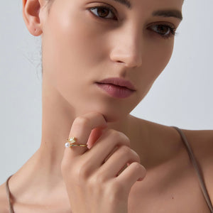 Woman wearing a gold ring with a pearl on a neutral background